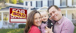 mortgage-loans family smiling in front of sold sign and house