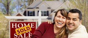 Couple smiling in front of sold sign and house 1