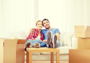 a man and woman sitting on a couch surrounded by moving boxes.